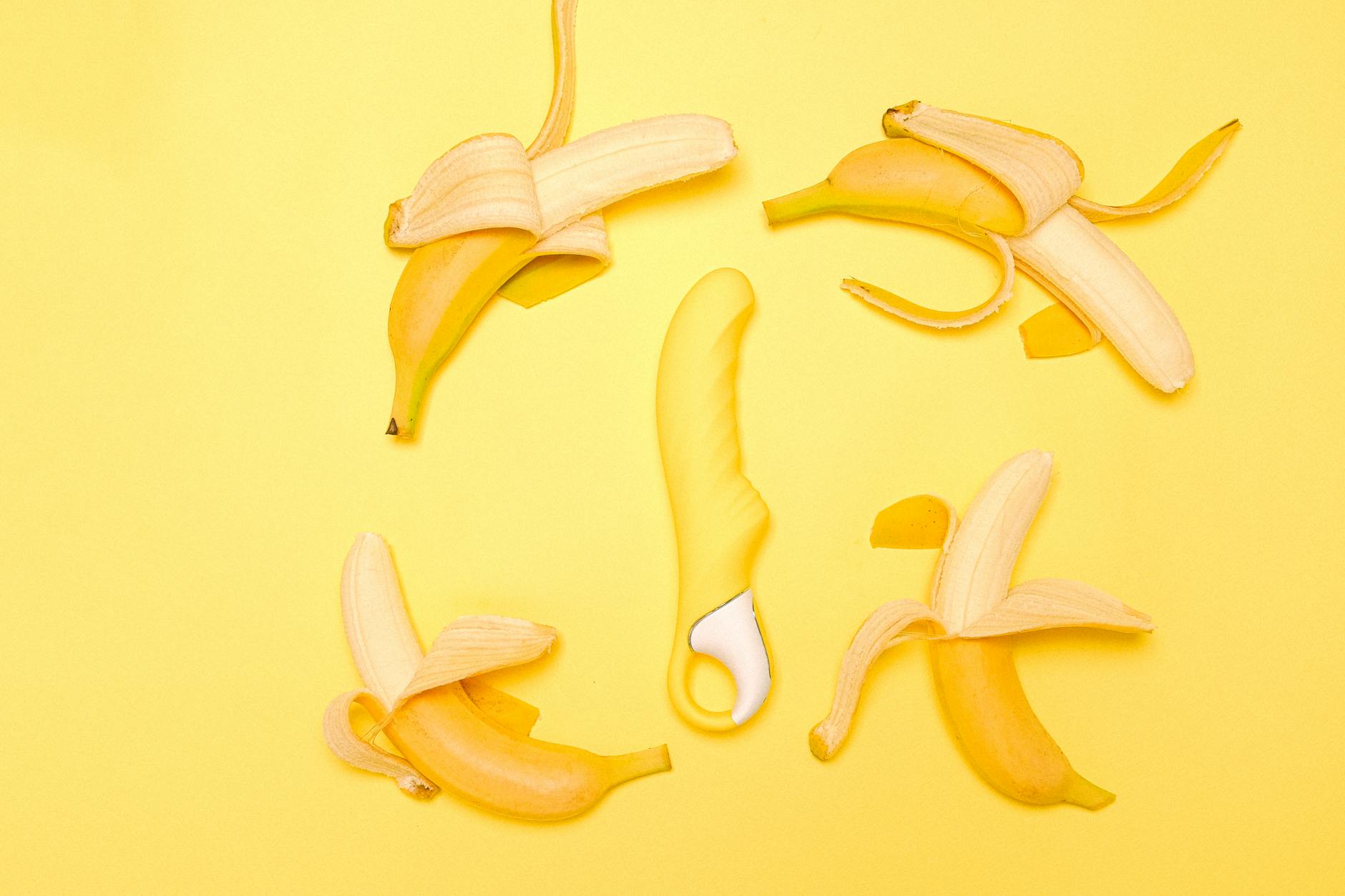 Žlutý silikónový vibrator obklopený loupanými citrony na žlutém pozadí