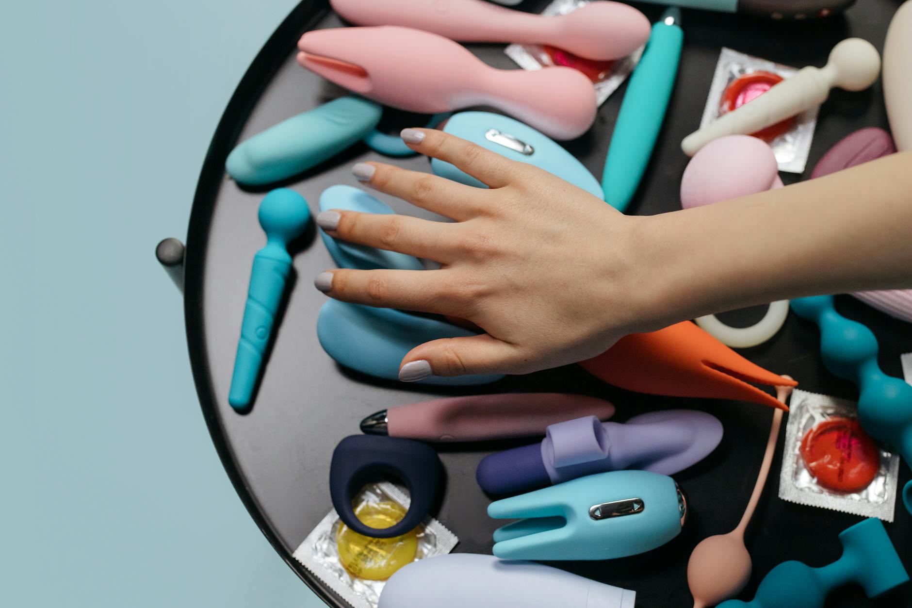 Ruka drží fialový vibrator na minimalistickém pozadí, symbolizující moderní sexualitu a intimitu
