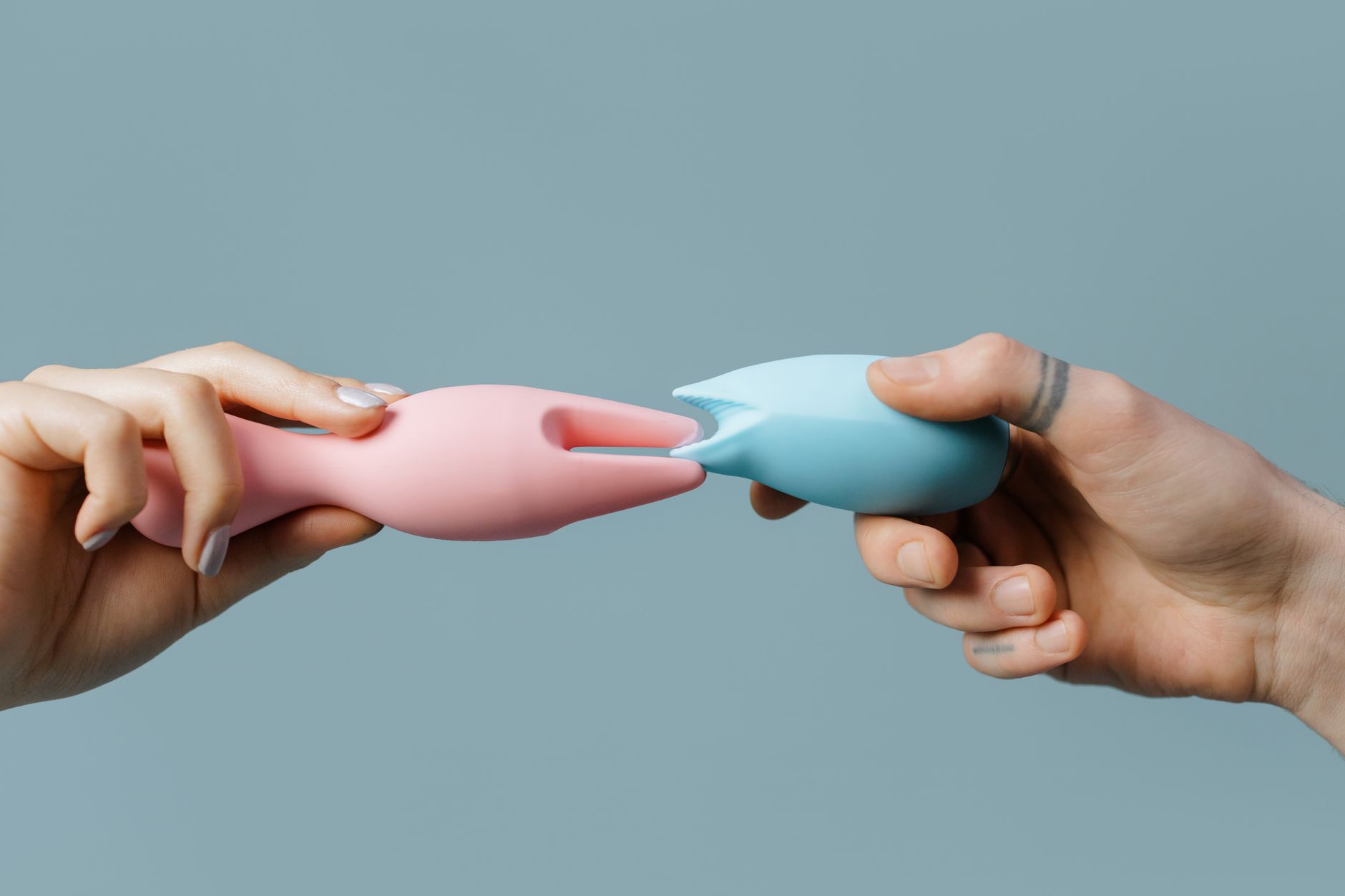 Ruka držící oranžový vibrator na minimalistickém purpurovém pozadí