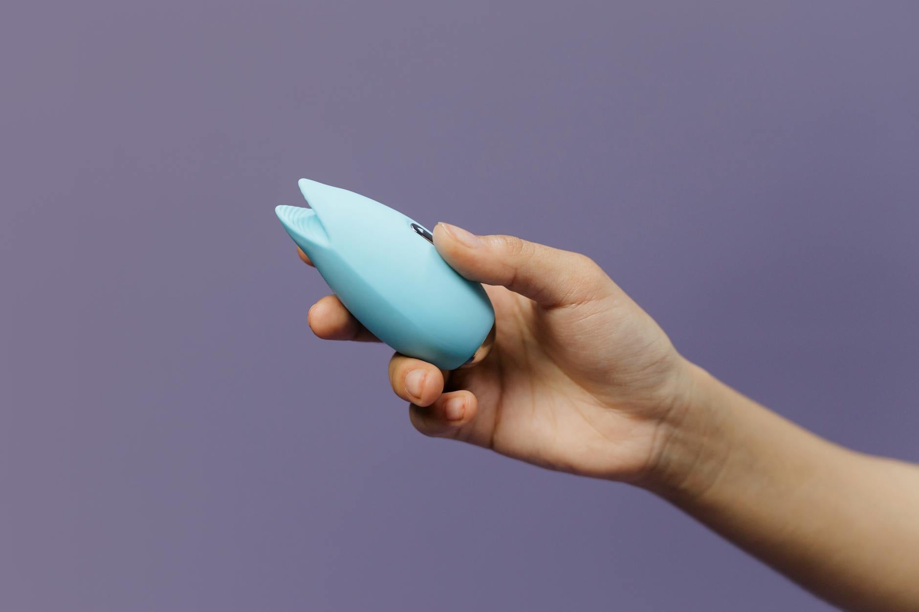 Modrý klitorální vibrator Lemon v ruce proti fialovému pozadí, podporující sebelásku a sexuální zdraví